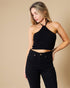 Woman wearing a black halter top and black pants against a beige background