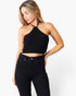 A woman modeling a black ribbed halter crop top paired with black jeans against a plain white studio background.