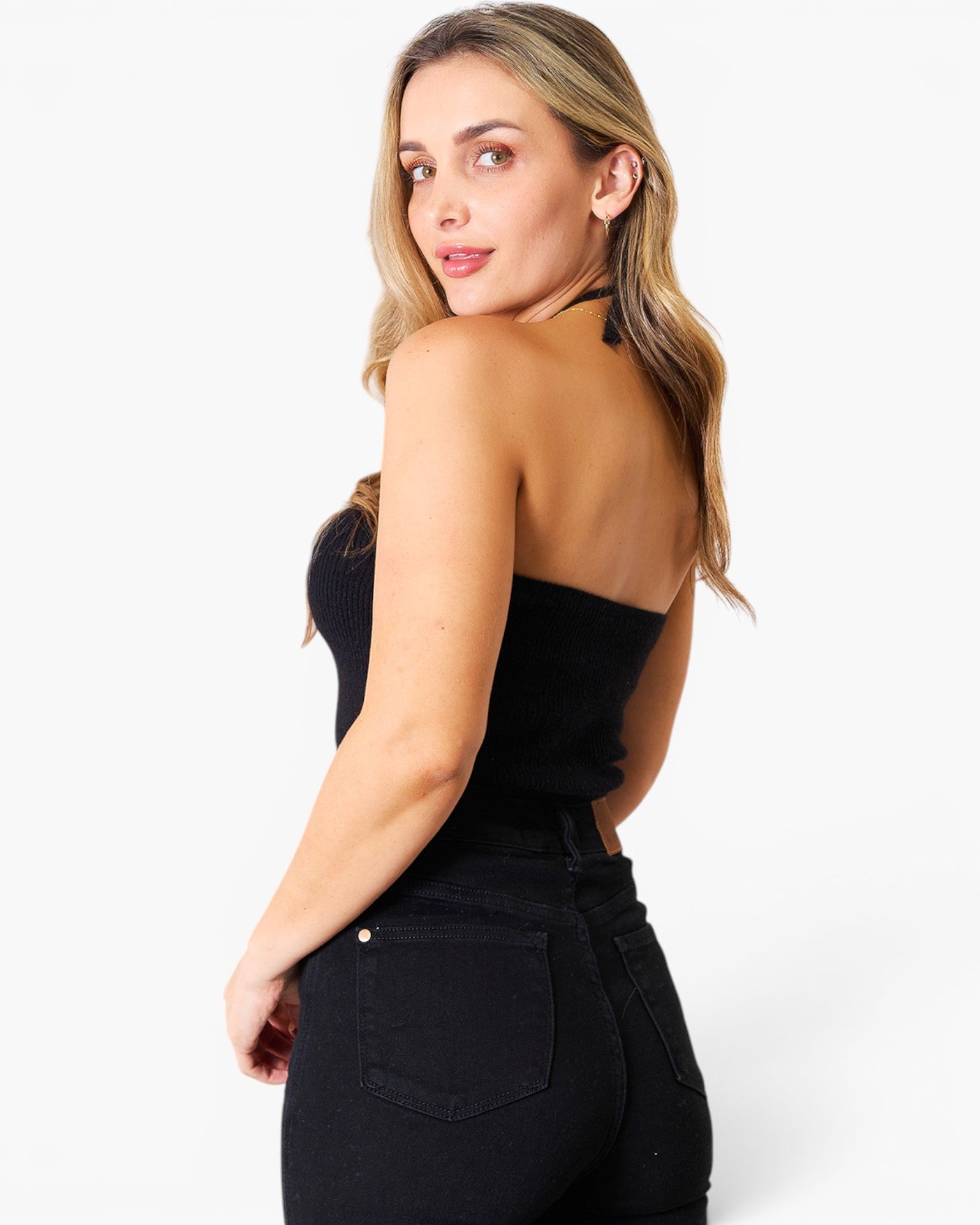 A woman wearing a black strapless bandeau top and black jeans, photographed from the back against a clean white studio background.
