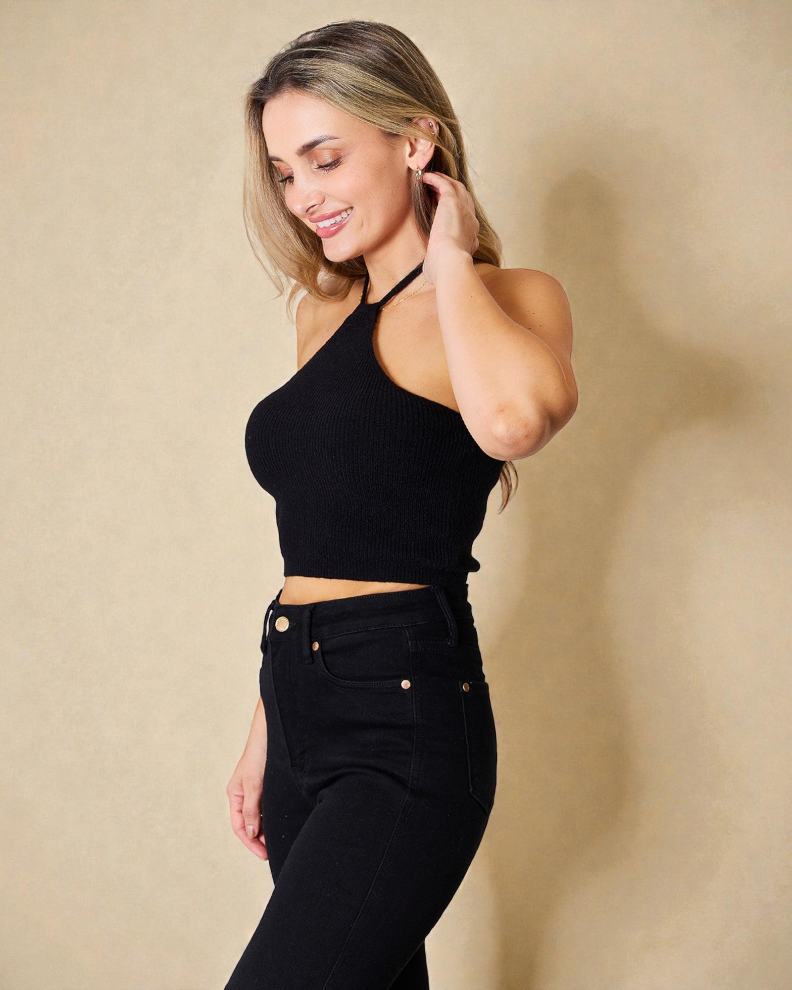 Woman wearing a black halter top and high-waisted black pants against a beige background