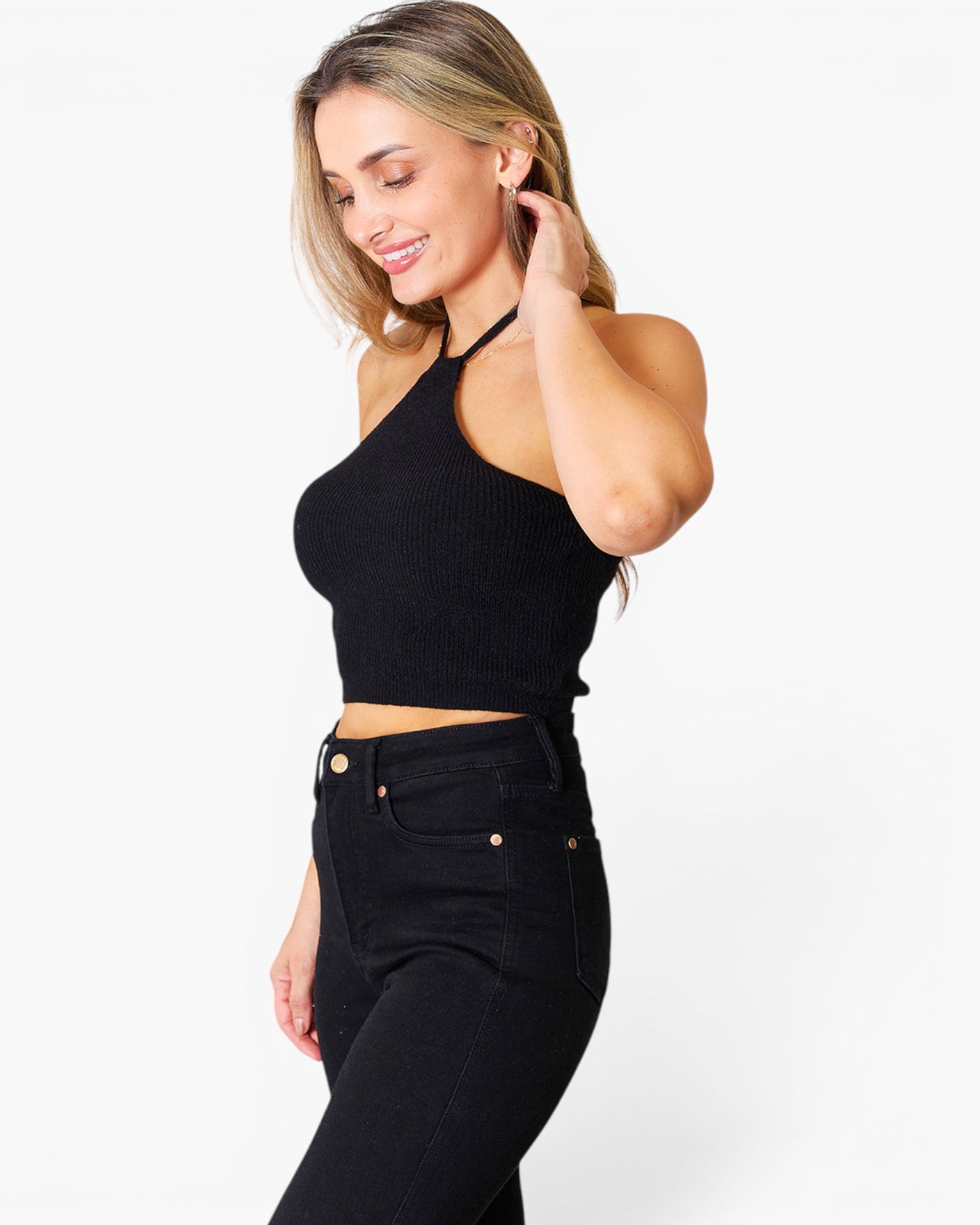 A woman wearing a black ribbed halter crop top and black jeans, posing against a solid white studio background.