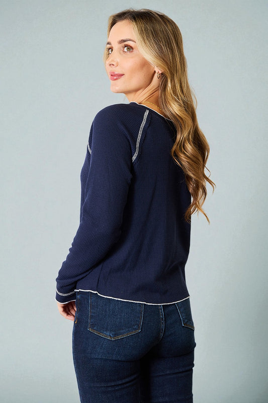 Woman wearing a navy blue sweater and jeans against a gray background