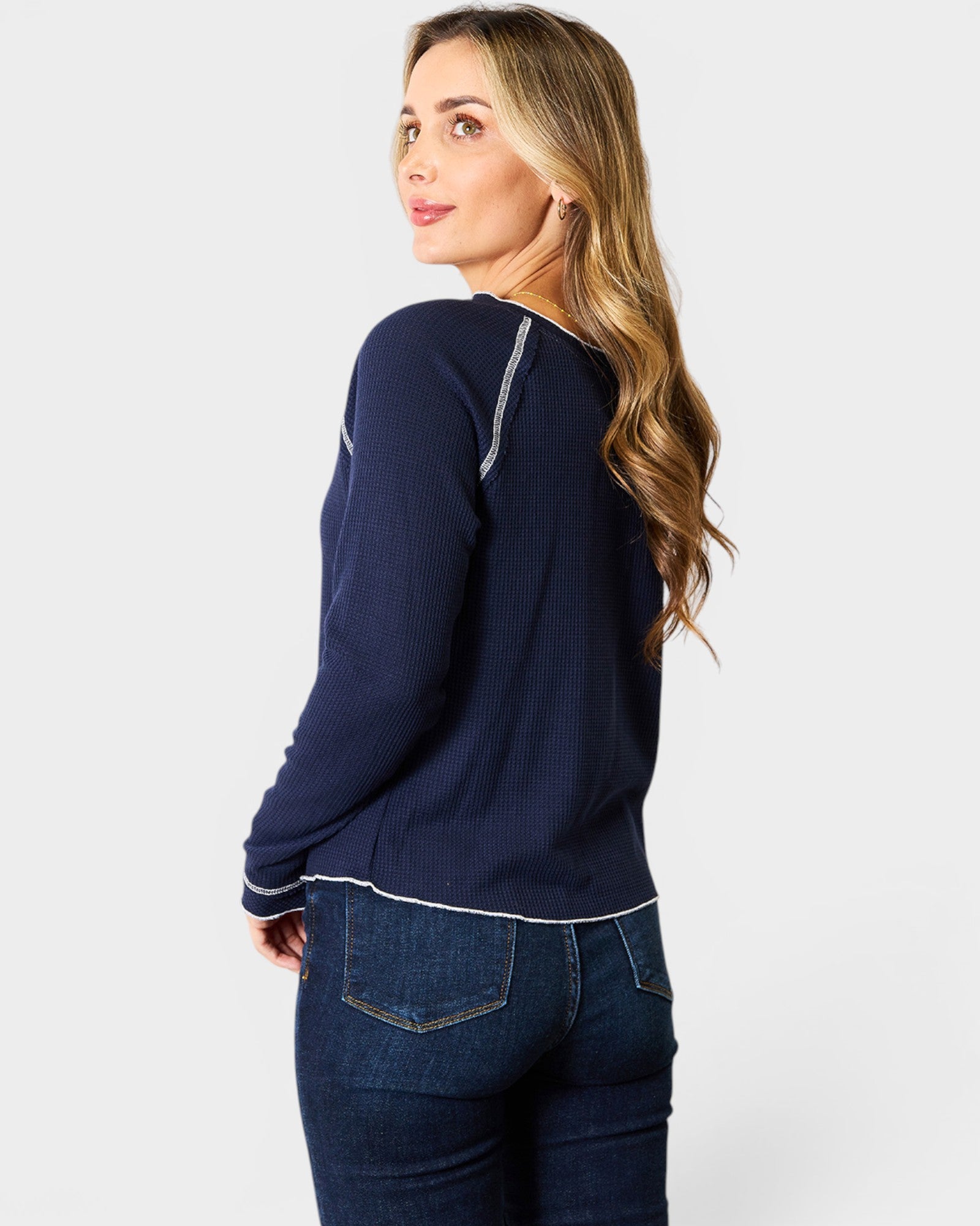 Woman wearing a navy sweater and blue jeans on a white background