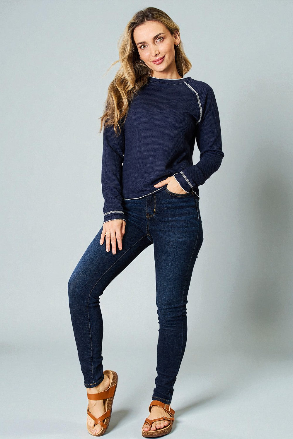 Woman wearing a navy sweater and jeans on a gray background