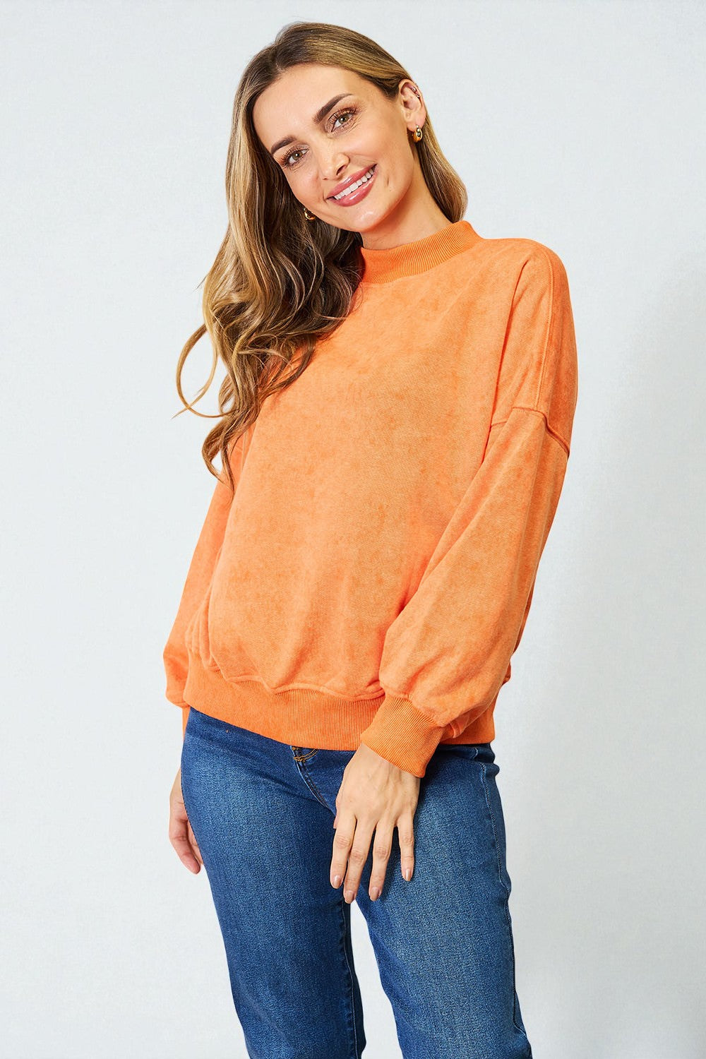 Woman wearing an orange sweater and blue jeans on a light gray background