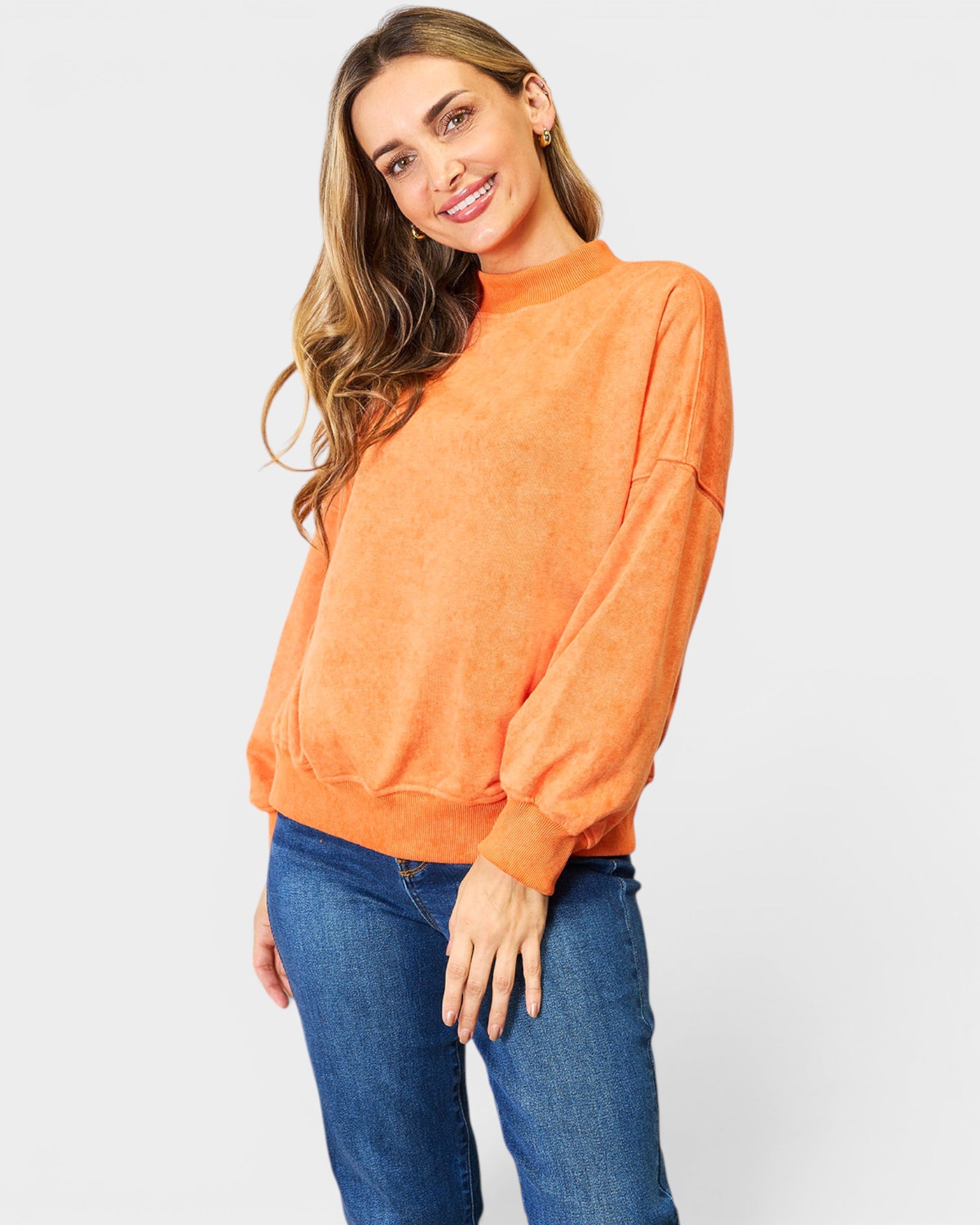 Woman wearing an orange sweater and blue jeans on a white background