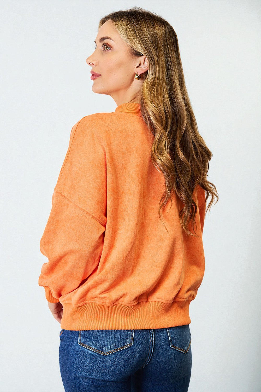 Woman wearing an orange sweatshirt and blue jeans against a white background