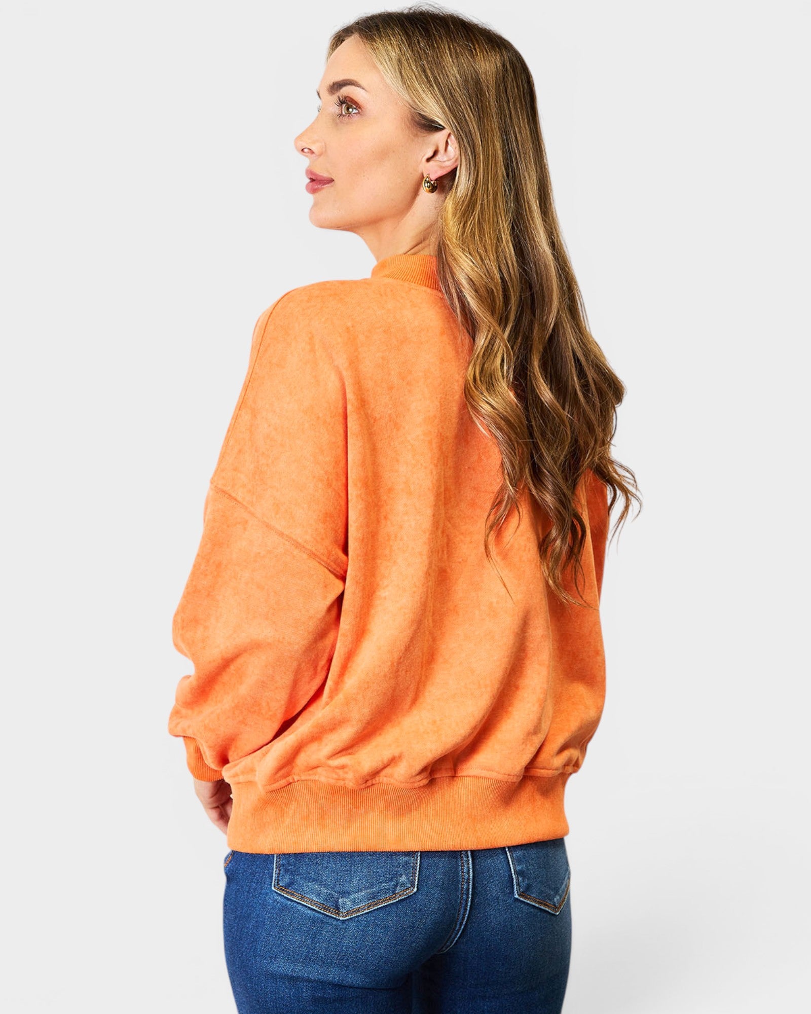 Woman wearing an orange sweatshirt and blue jeans on a white background