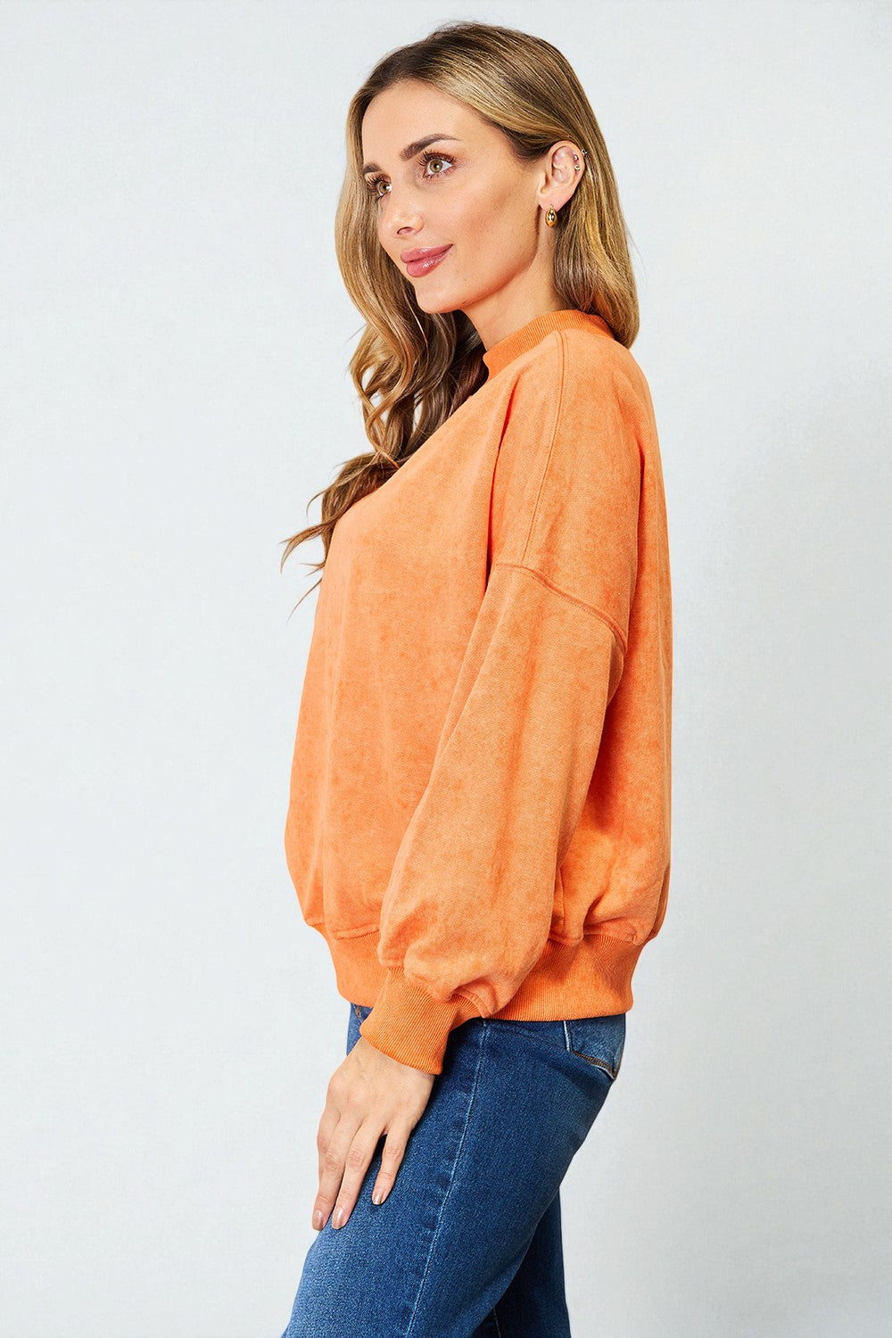 Woman wearing an orange sweater and blue jeans against a white background
