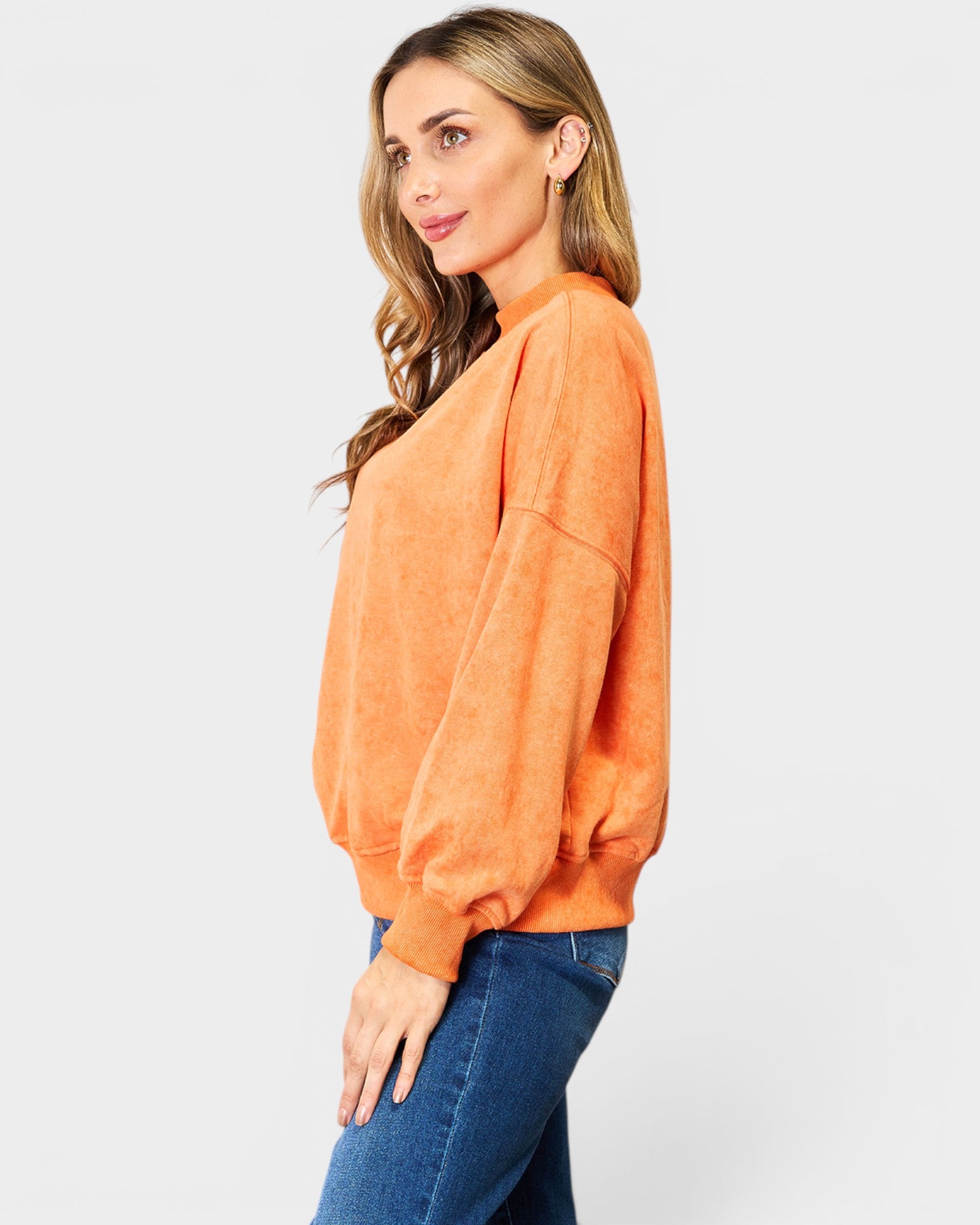 Woman wearing an orange sweatshirt and blue jeans on a white background