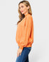 Woman wearing an orange sweatshirt and blue jeans on a white background