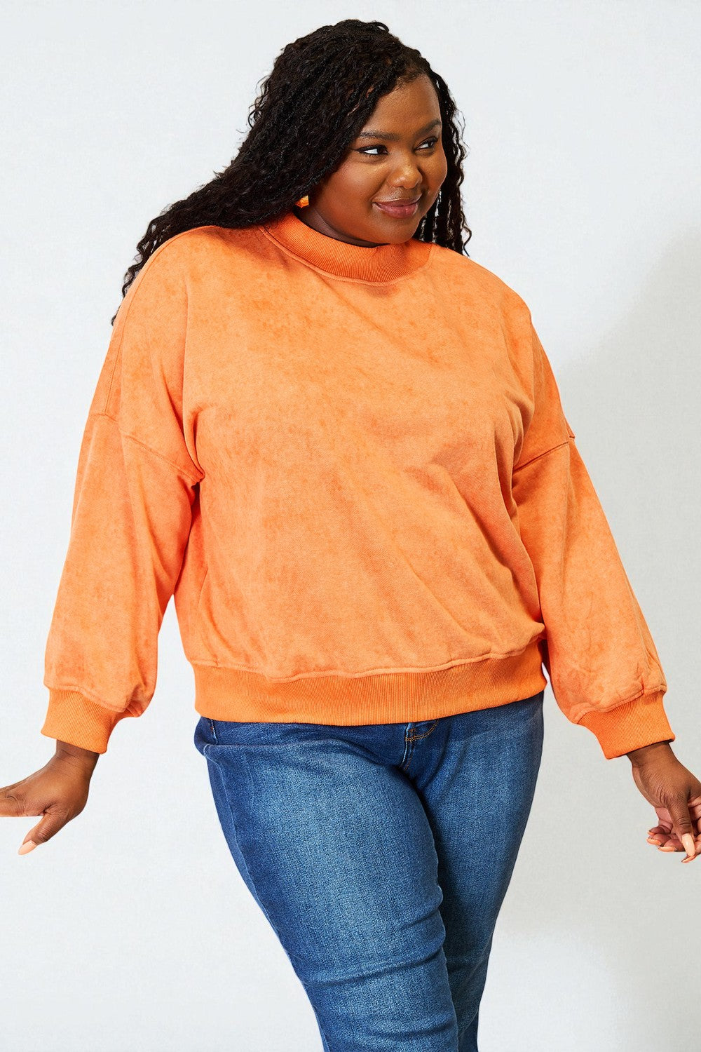 Person wearing an orange sweatshirt and blue jeans on a white background