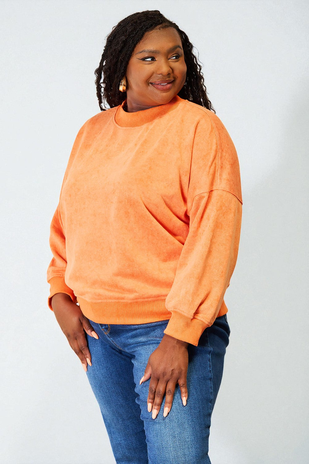 Woman wearing an orange sweatshirt and blue jeans against a white background