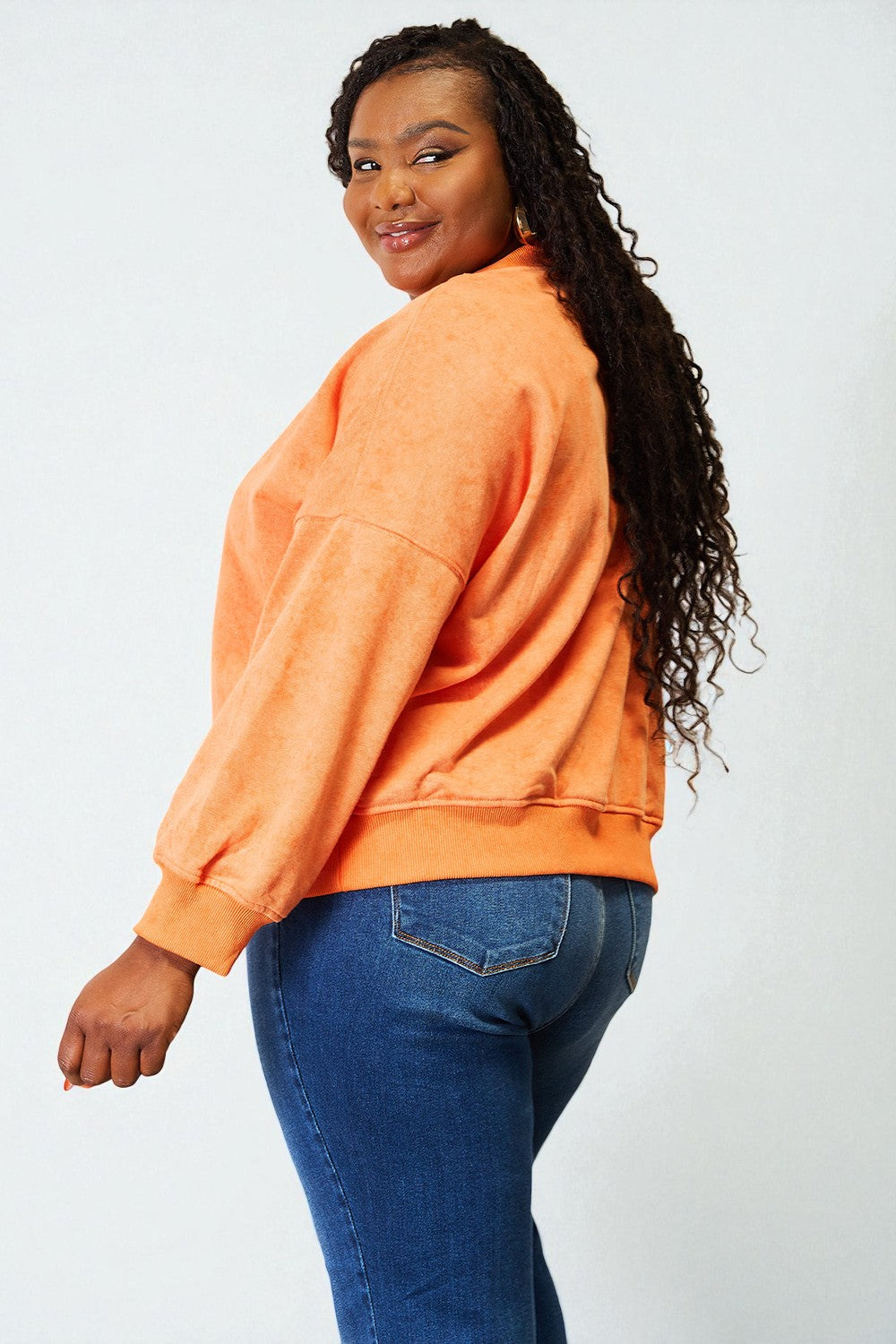 Person wearing an orange sweatshirt and blue jeans on a white background