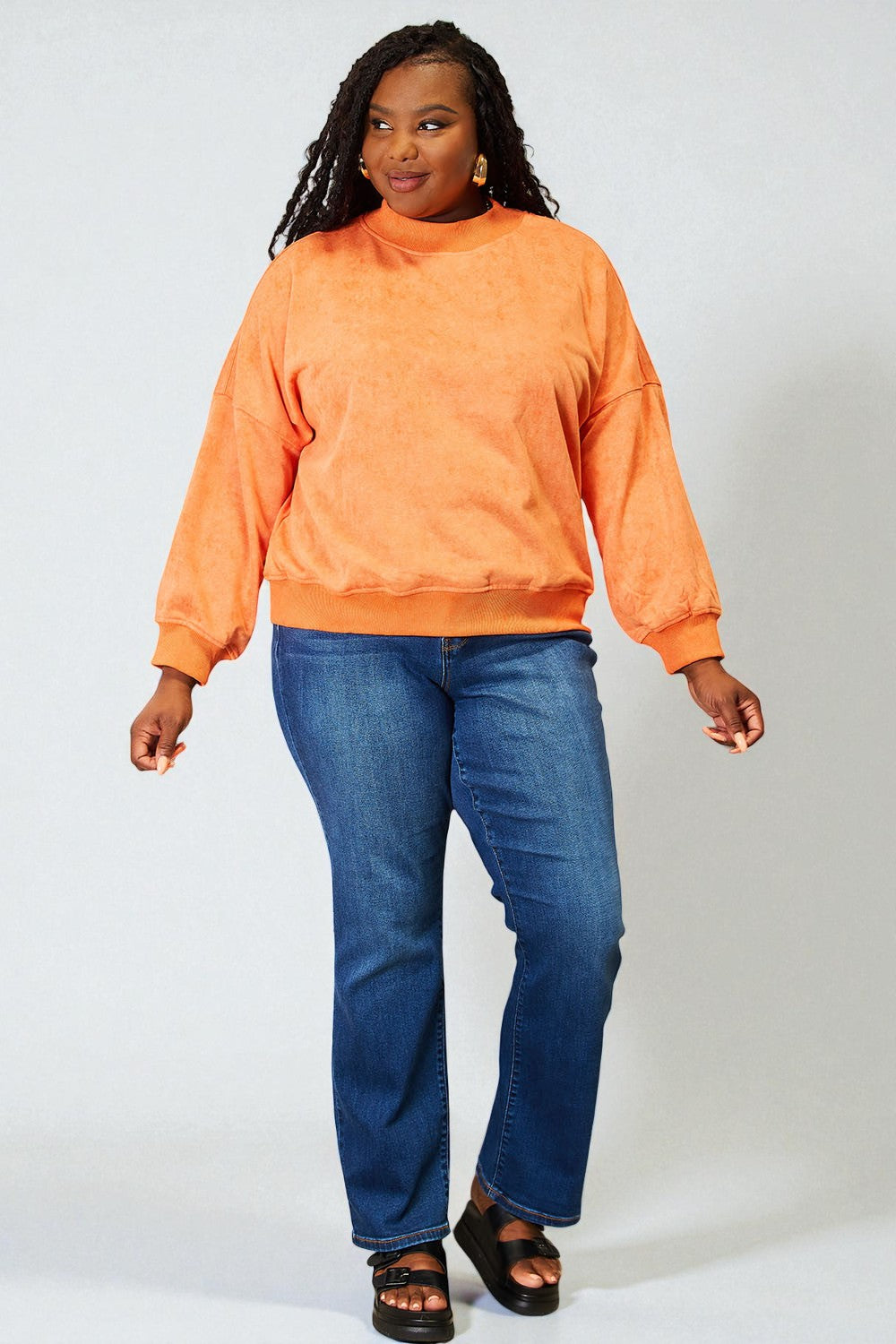 Person wearing an orange sweatshirt and blue jeans on a white background
