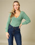 Woman wearing a green sweater and blue jeans against a beige background