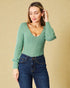 Woman wearing a green ribbed sweater and blue jeans against a beige background