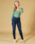 Woman wearing a green sweater and blue jeans against a beige background