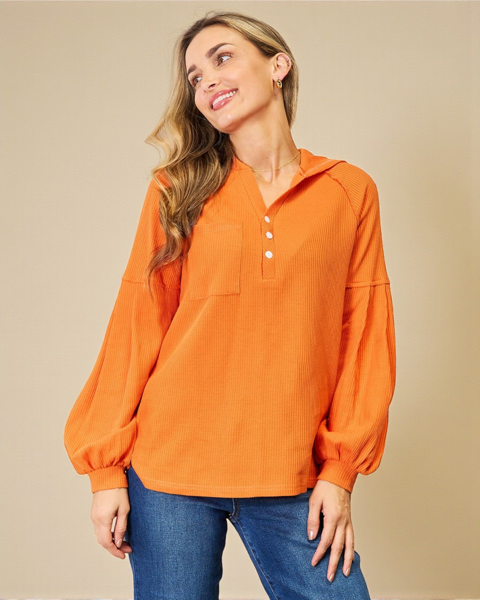 Woman wearing an orange long-sleeve shirt with a beige background