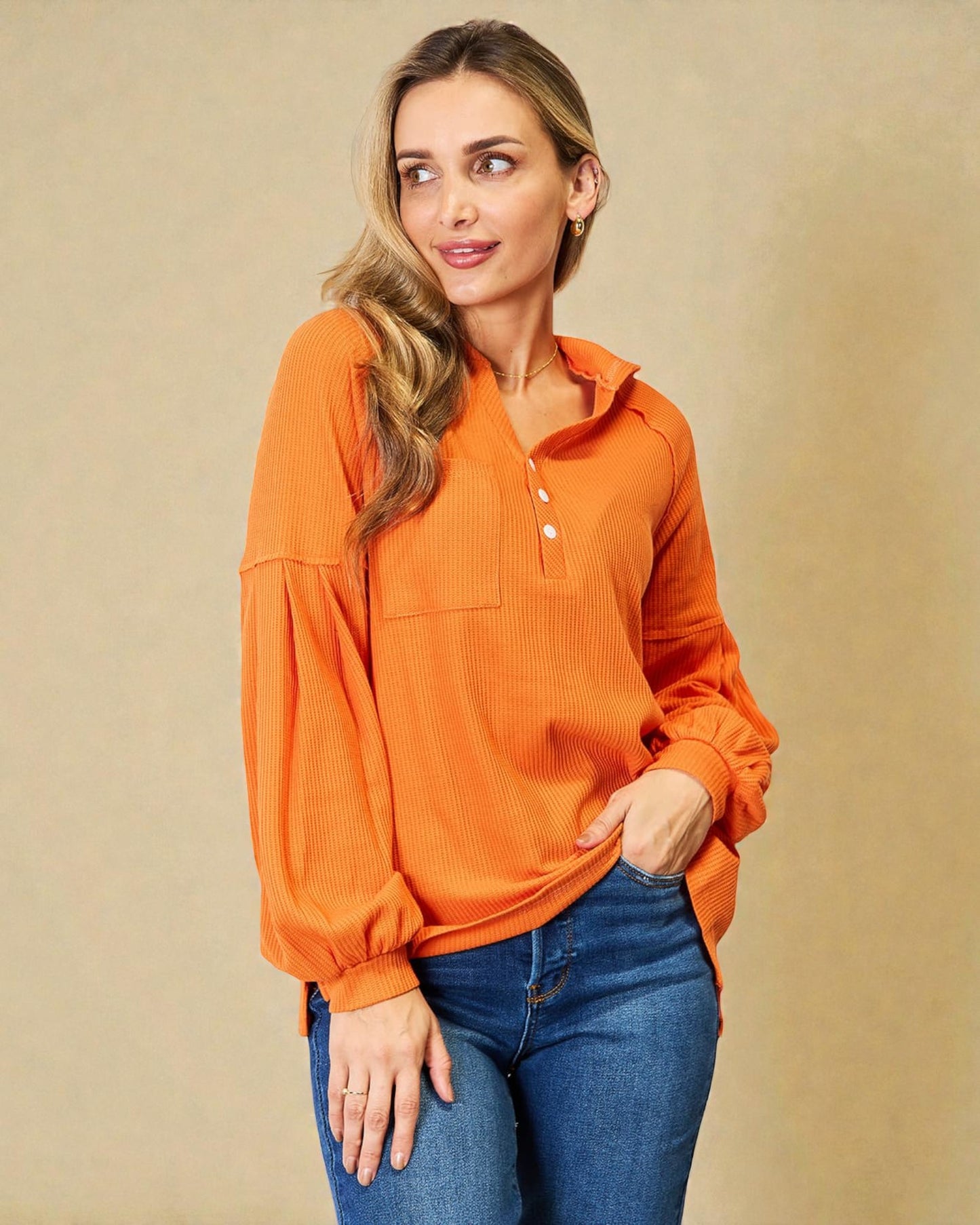 Woman wearing an orange long-sleeve shirt and blue jeans against a beige background