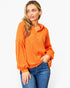 A woman wearing a bright orange long-sleeve ribbed knit top with a partial button placket and chest pocket, paired with blue jeans, against a plain white background.