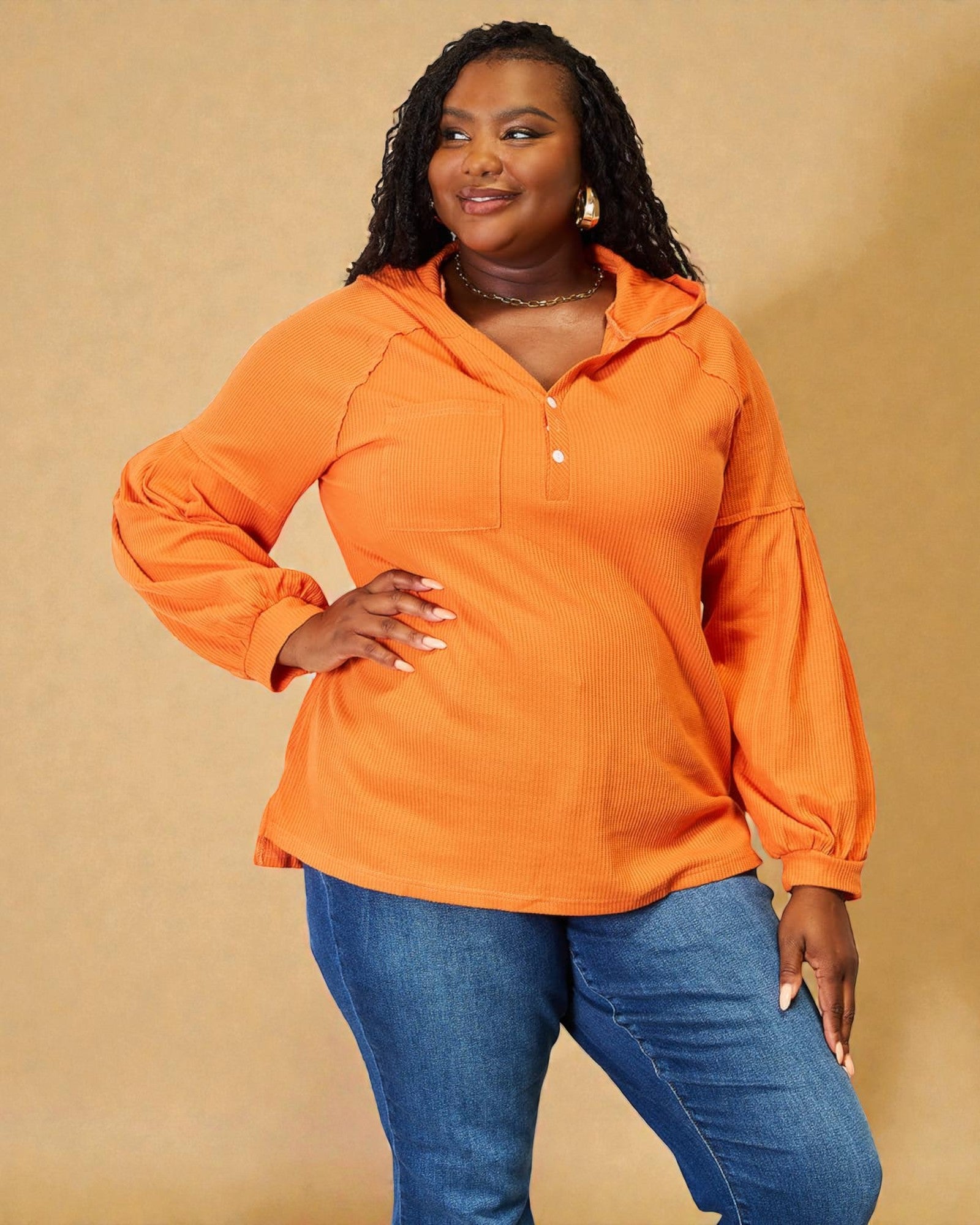 Woman wearing an orange long-sleeve shirt and blue jeans against a beige background