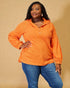 Woman wearing an orange long-sleeve shirt and blue jeans against a beige background
