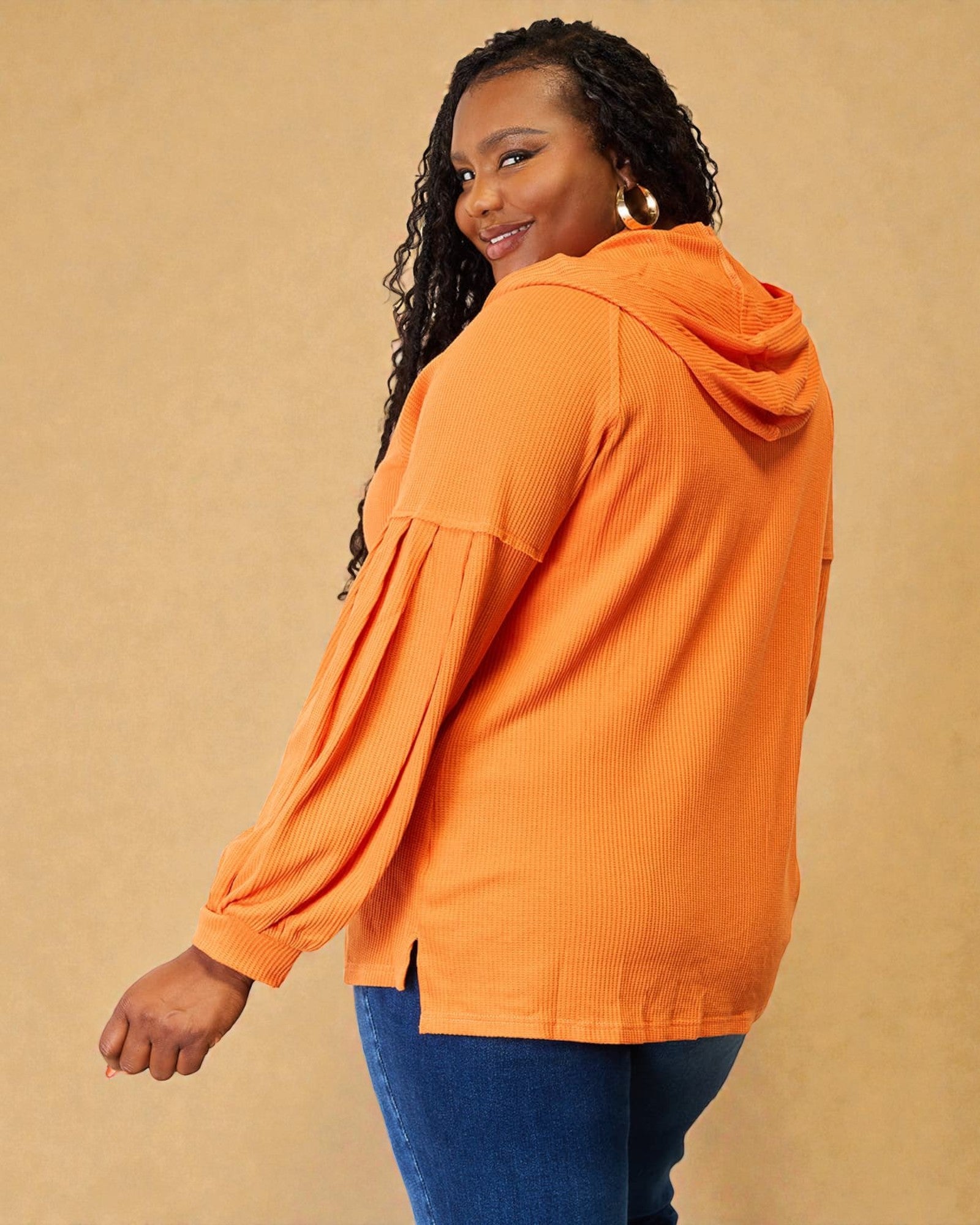 Woman wearing an orange hooded jacket against a beige background