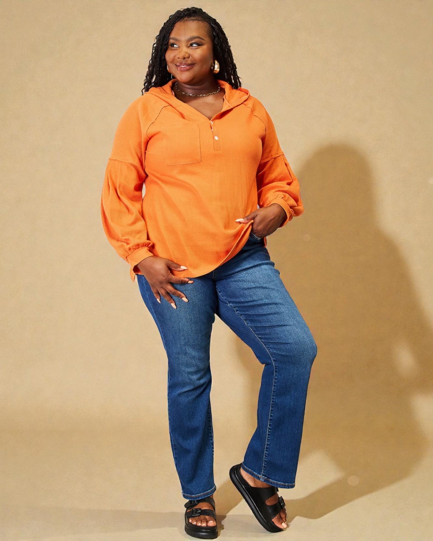 Woman wearing an orange hoodie and blue jeans against a beige background