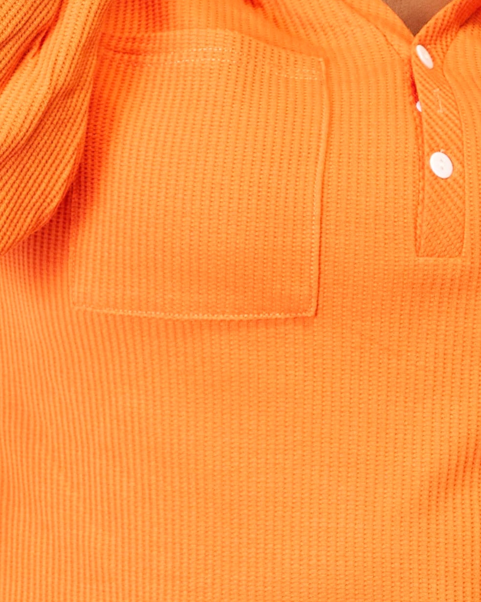 Close-up of an orange textured knit polo shirt showing a chest pocket and partial button placket.