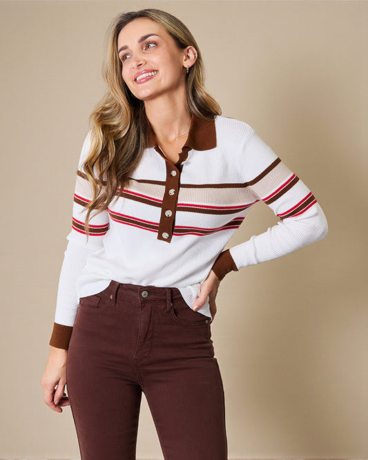 Woman wearing a white sweater with brown and red stripes and brown pants on a beige background