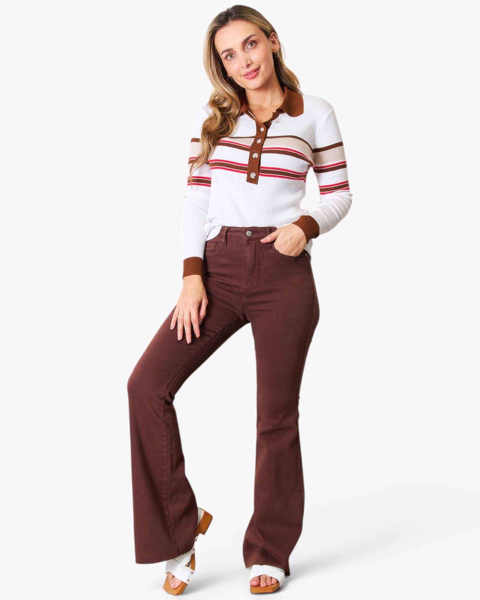 A woman modeling a white long-sleeve polo shirt with brown and red horizontal stripes, paired with high-waisted brown flare jeans and white heeled sandals, against a light gray studio background.
