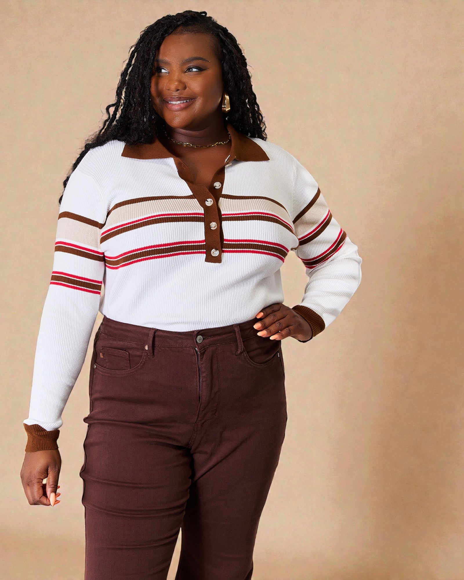 Woman wearing a white sweater with brown and red stripes and brown pants against a beige background