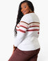 A woman wearing a white ribbed knit sweater with brown and red striped details on the sleeves and shoulders, paired with brown pants, photographed against a clean white background.