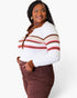 A woman modeling a white ribbed knit polo-style top with brown and red horizontal stripes, paired with brown pants, against a light gray studio background.