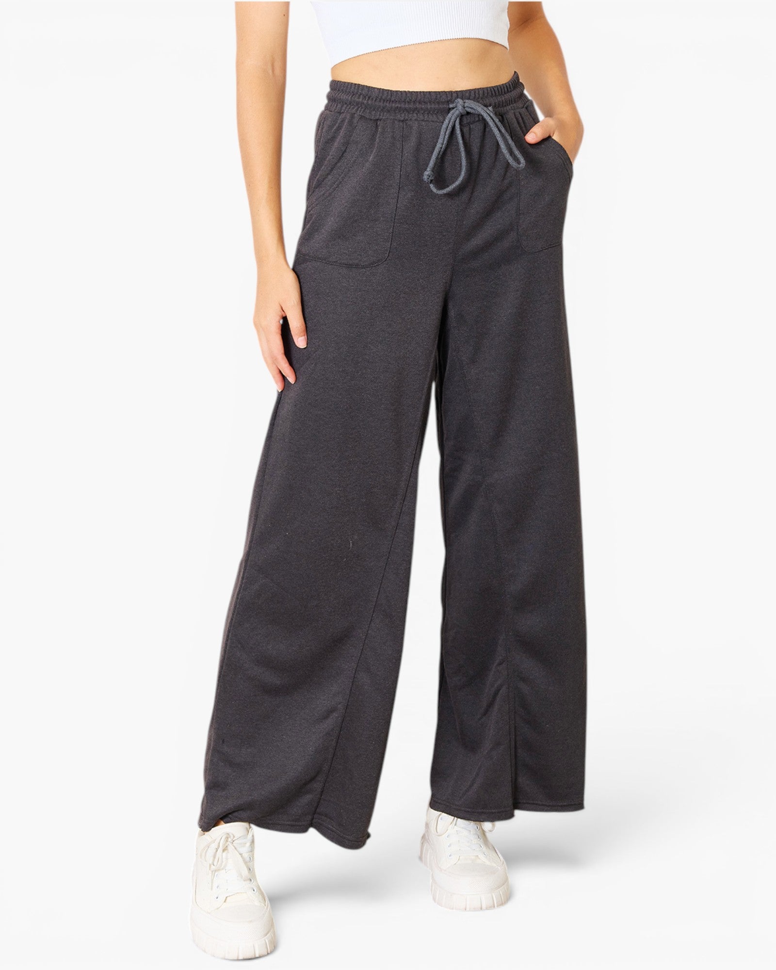 A person wearing dark charcoal wide-leg sweatpants with an elastic drawstring waist, paired with white sneakers against a clean white studio background.