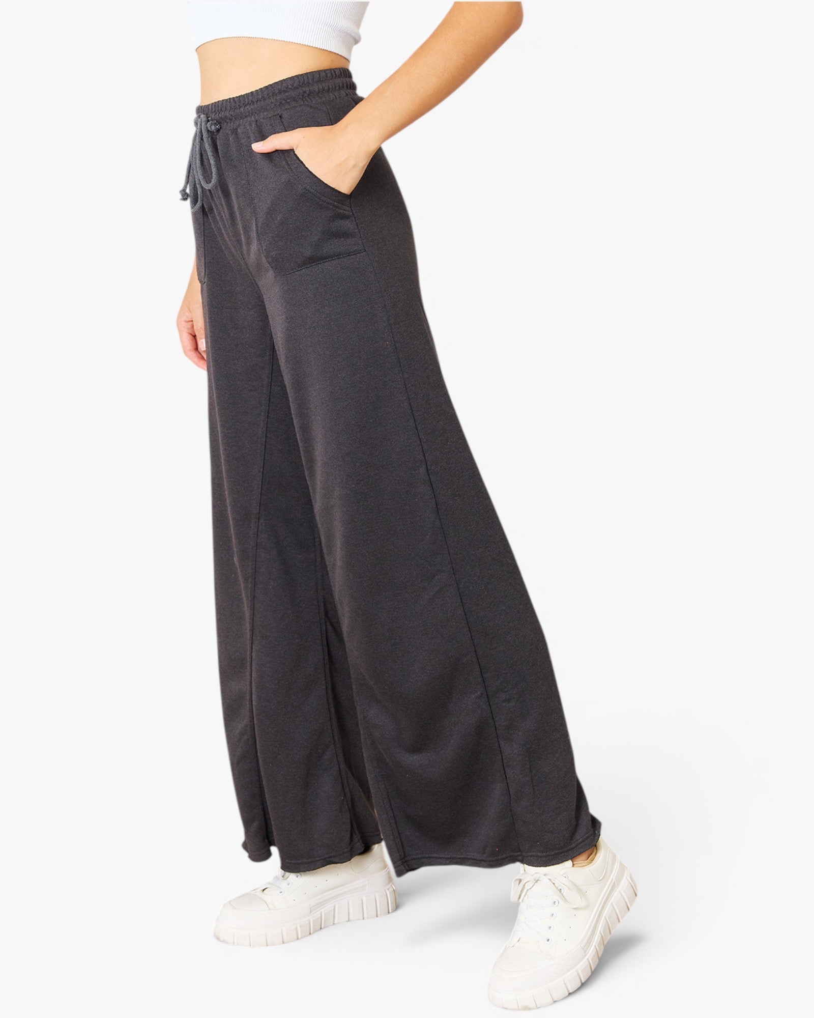 A person wearing dark charcoal wide-leg sweatpants with a drawstring waistband, paired with white sneakers, shown against a plain white studio background.