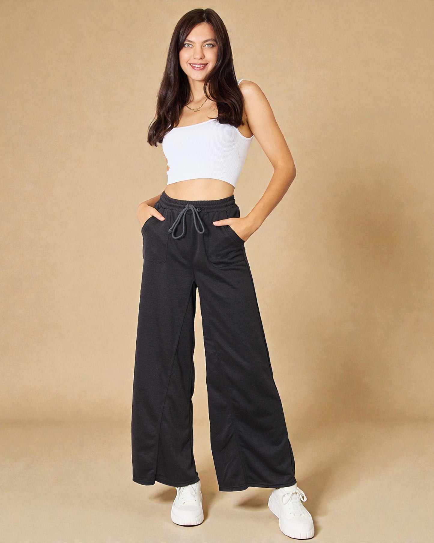 Woman wearing a white crop top and black wide-leg pants on a beige background