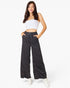 A woman modeling a pair of wide-leg charcoal gray drawstring pants with a white strapless crop top and white sneakers, standing against a solid white studio background.