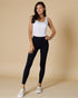 Woman wearing a white tank top and black leggings on a beige background