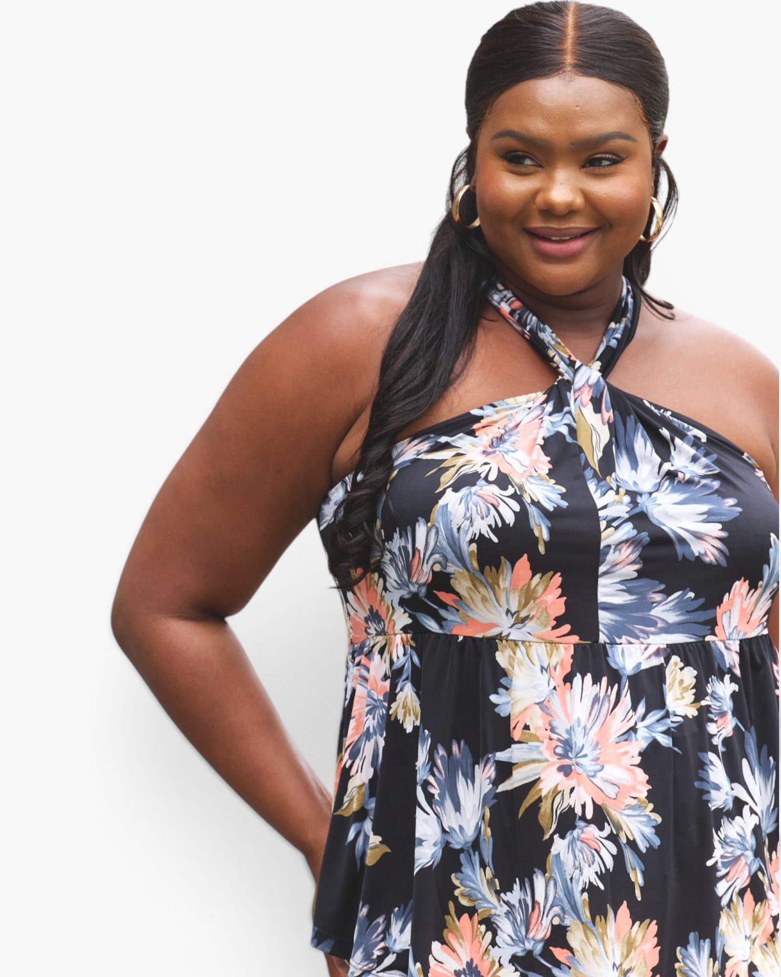 A woman wearing a halter-neck floral dress with a black base and multicolor watercolor-style flowers in blue, pink, and peach, photographed against a plain light gray background.