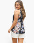 A woman modeling a sleeveless halter-style top with a dark navy floral print and white shorts against a plain light gray background.