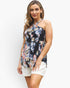 A woman modeling a sleeveless halter-neck top with a dark navy floral print in pink, blue, and white, paired with white shorts, against a light gray studio background.