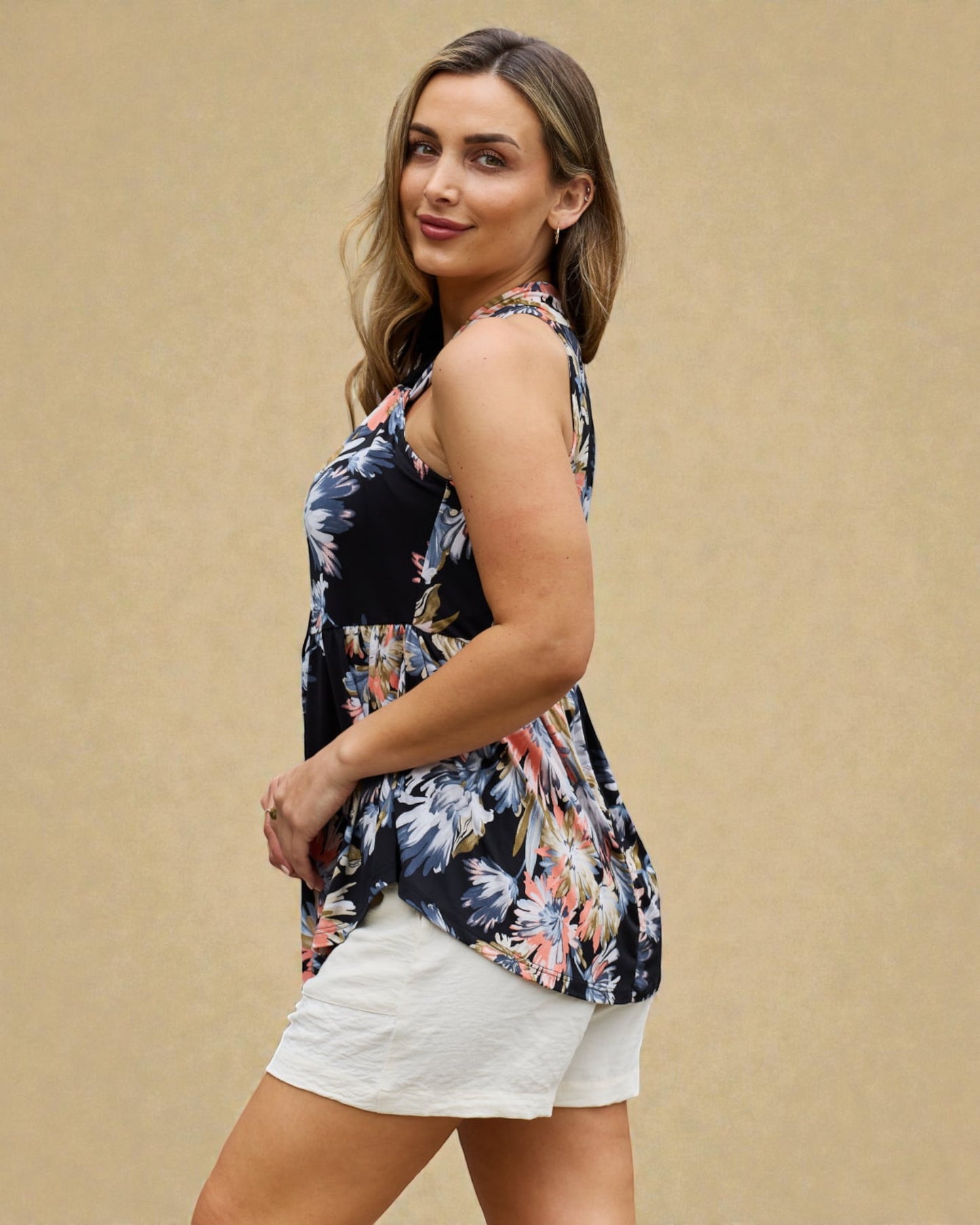 Woman wearing a sleeveless floral top and white shorts against a beige background