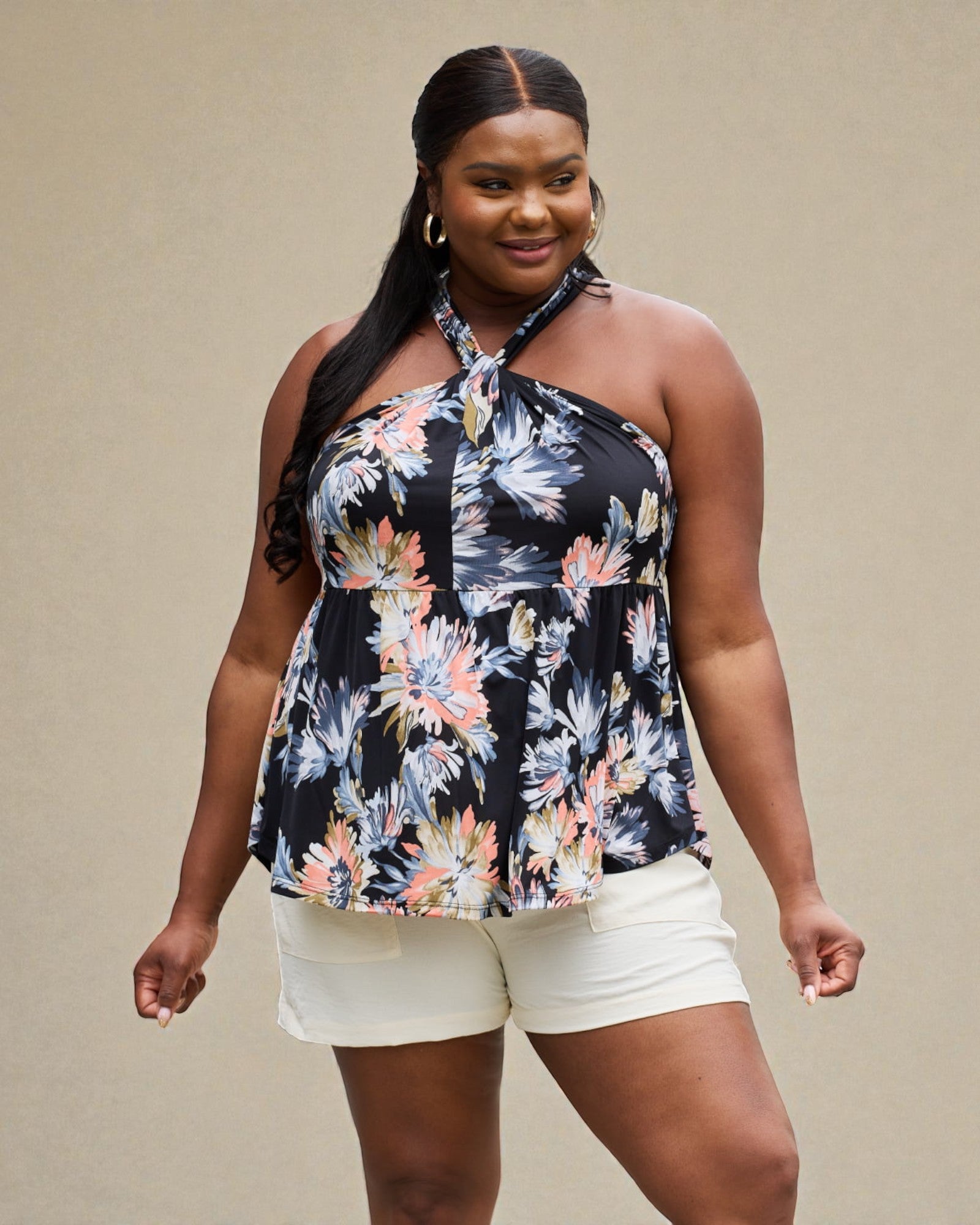 Woman wearing a floral halter top and white shorts against a beige background