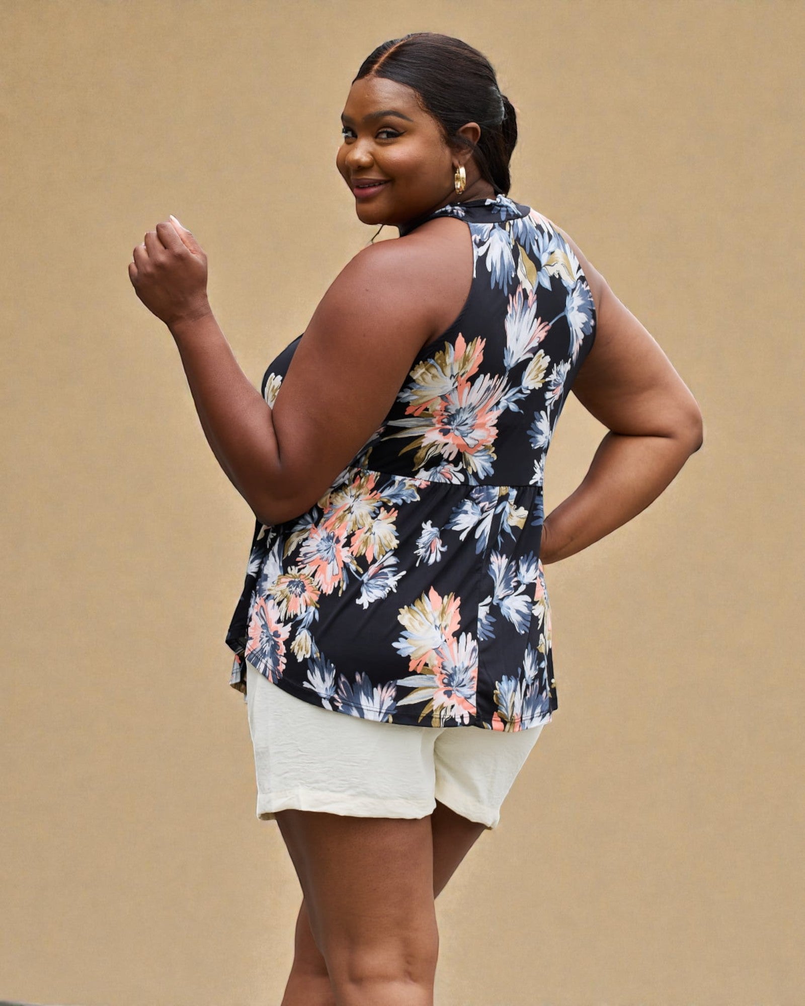 Woman wearing a floral sleeveless top and white shorts on a beige background