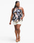 A woman modeling a plus-size halter top with a black base and a colorful floral print in pink, blue, and white, paired with white shorts and tan platform sandals, against a light gray studio background.