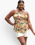 A woman modeling a halter-neck crop top with a colorful tropical floral and leaf print on a cream background, paired with white shorts, against a light gray studio background.