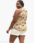 A woman modeling a sleeveless tropical floral print peplum top with white shorts, shown from a three-quarters back view against a plain white background.