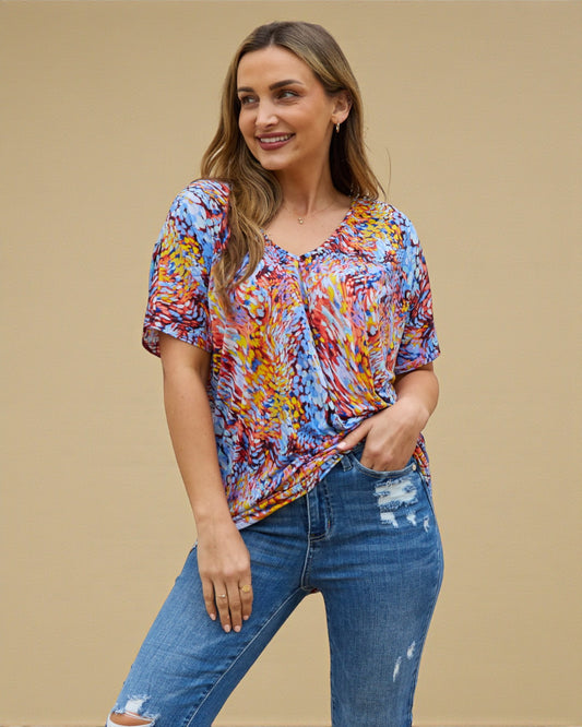 Woman wearing a colorful patterned top and blue jeans against a beige background